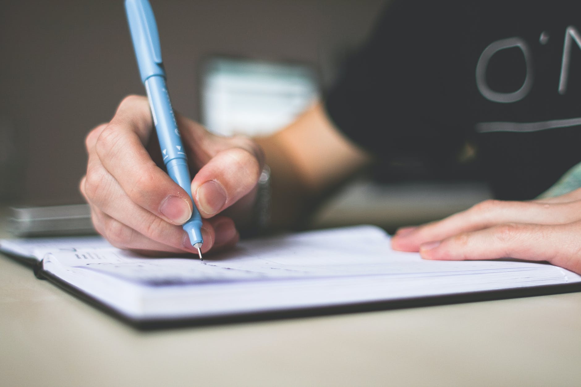 person holding blue ballpoint pen writing in notebook